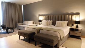 A modern hotel room with a large bed, two bedside tables, a sofa, and a small table with a vase.