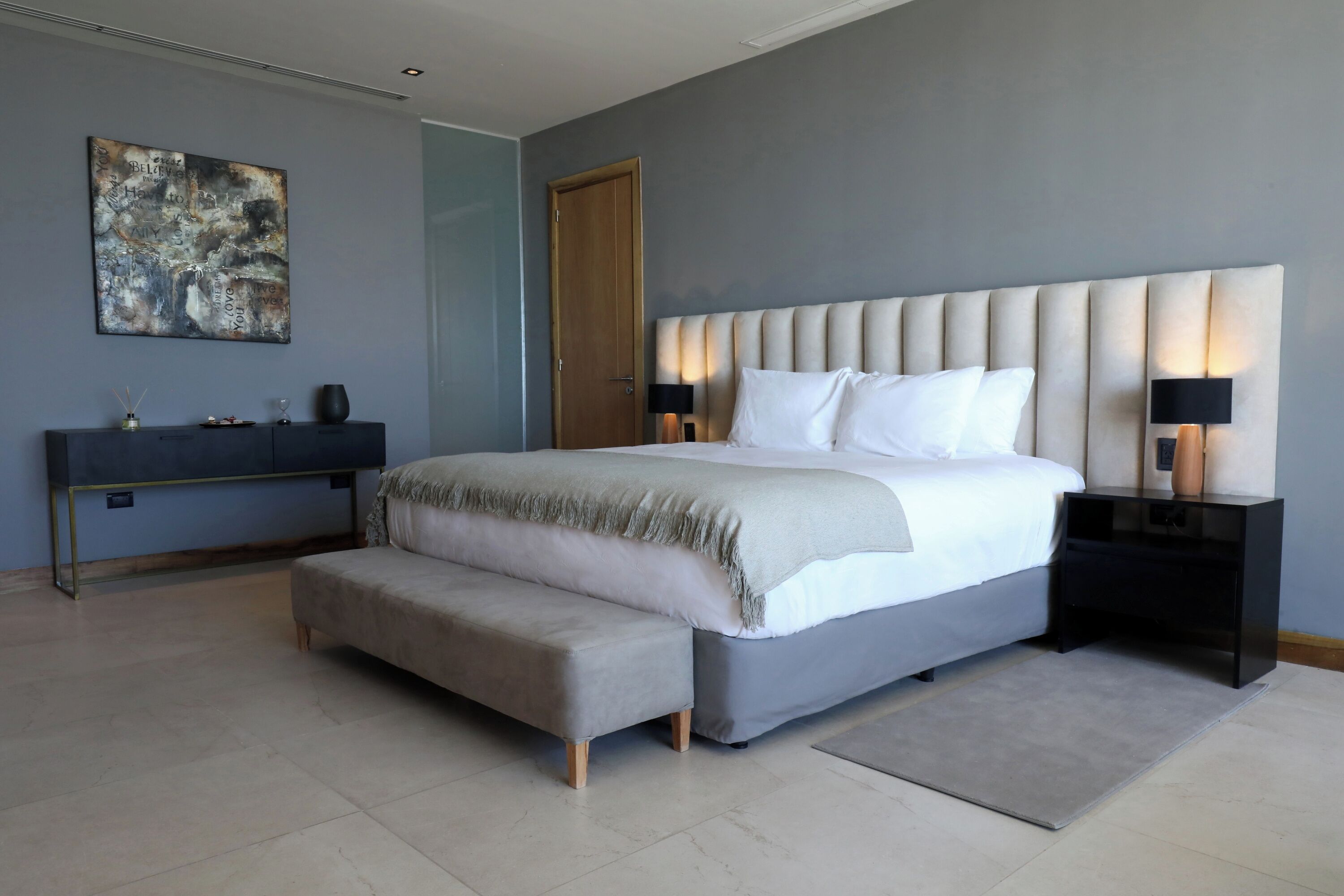 Un dormitorio moderno con una cama grande, mesitas de noche, una consola y un banco.