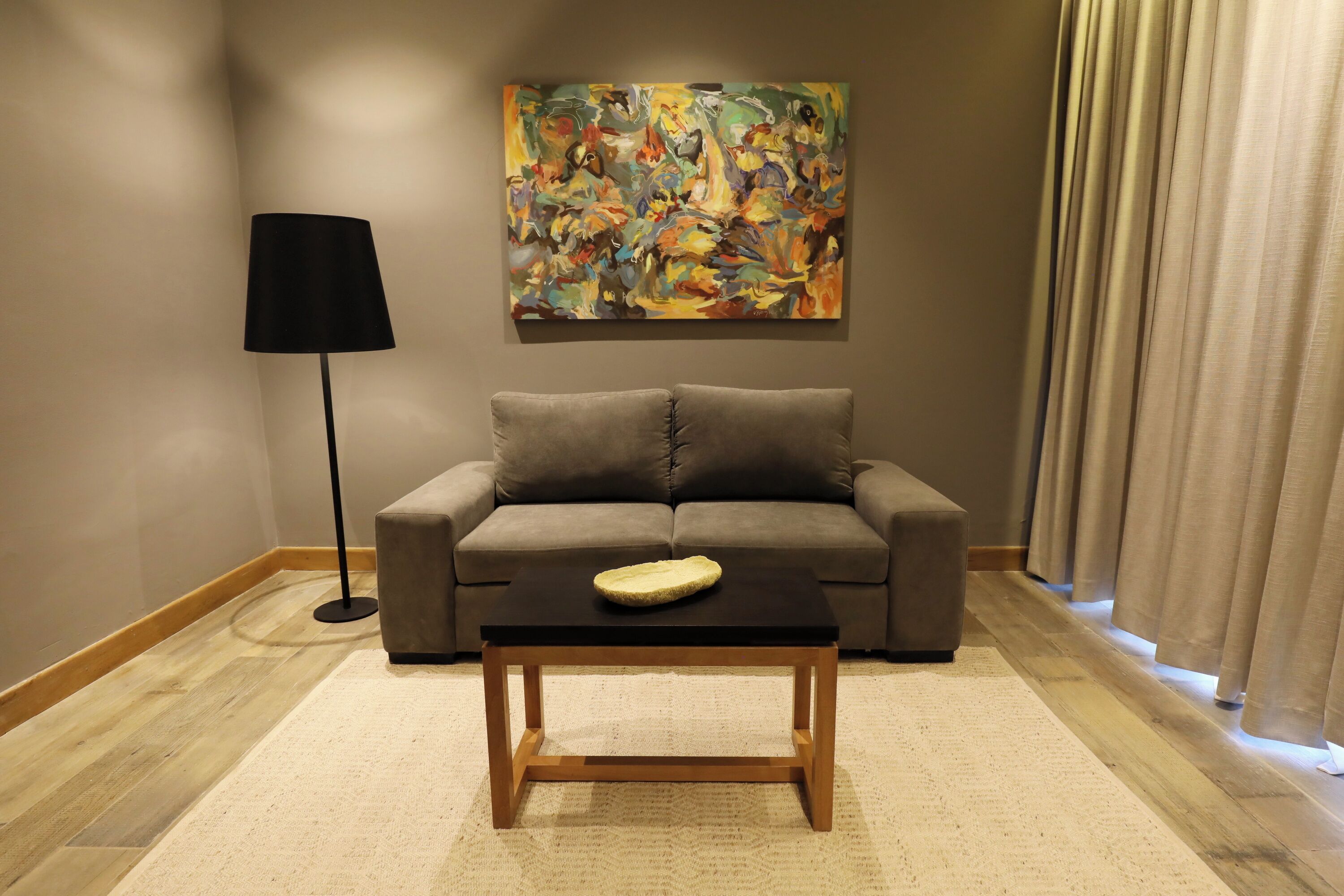 A living room with a sofa, a coffee table, a floor lamp, and a painting on the wall.