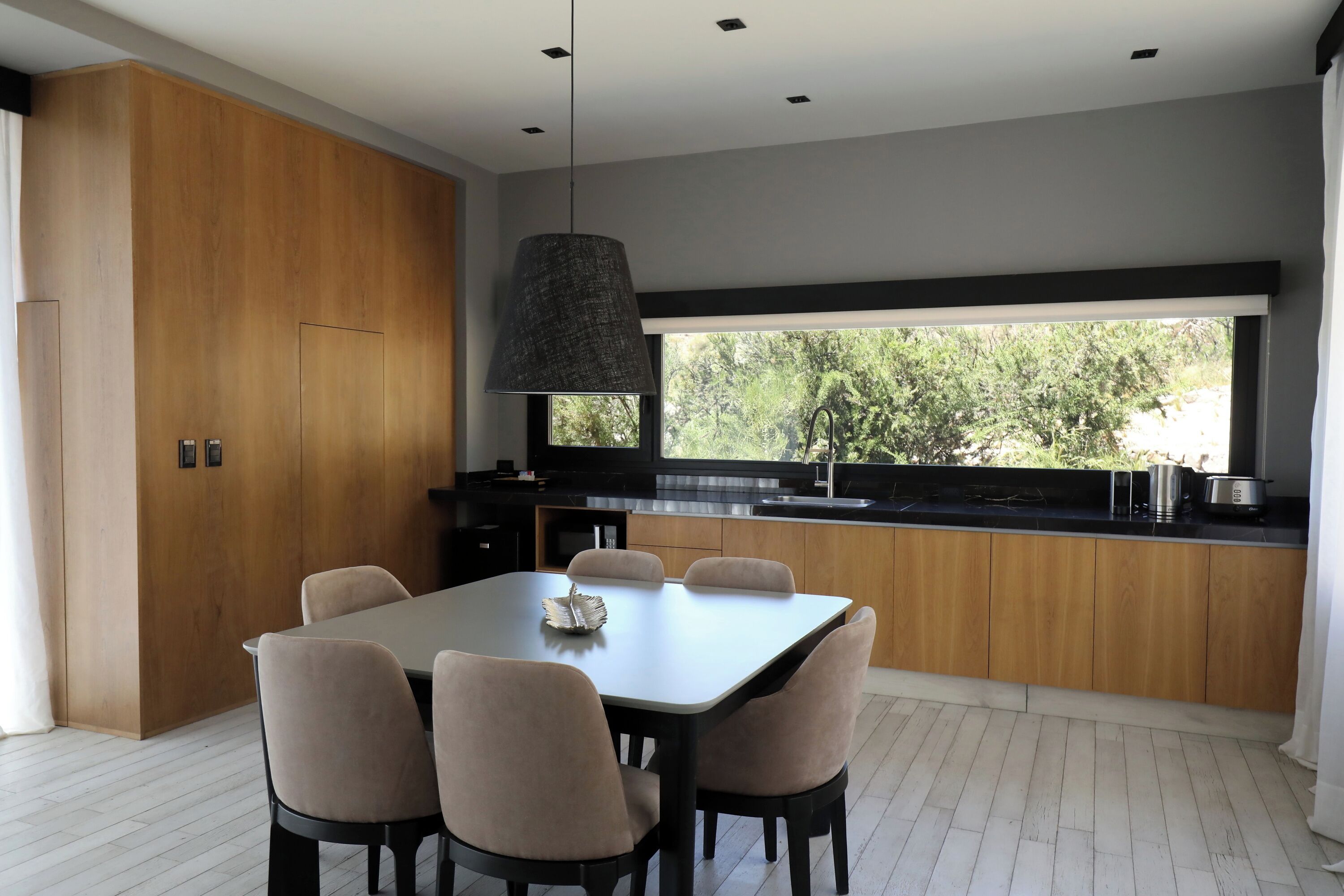 Una cocina moderna con comedor, que cuenta con un amplio ventanal, armarios de madera y una mesa de comedor con sillas.