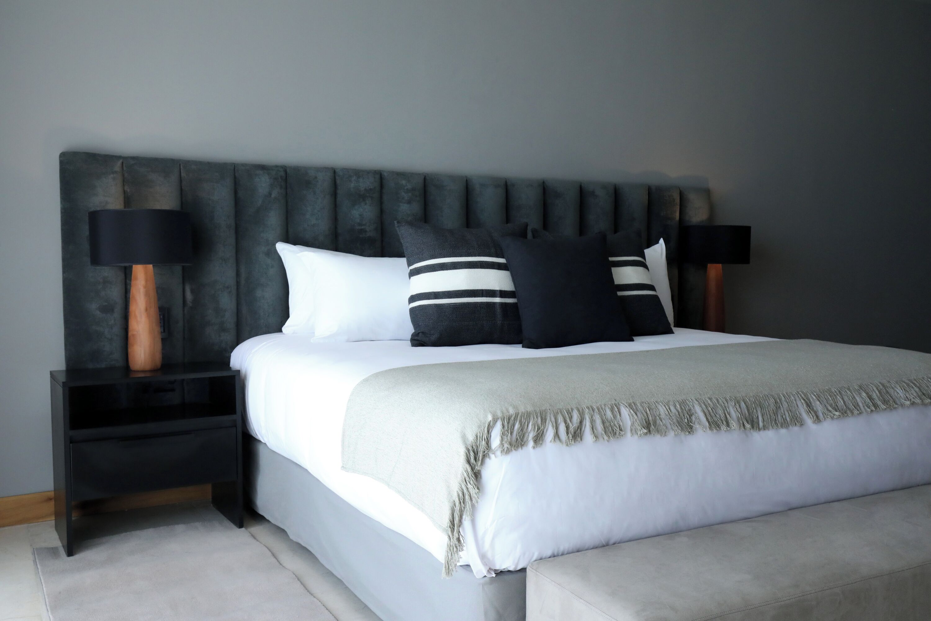 A bedroom with a bed, a nightstand, a lamp, and a headboard.