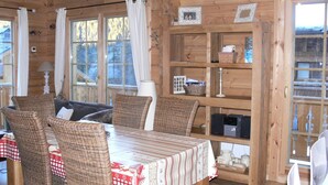 L’intérieur d’un chalet en bois chaleureux et accueillant, avec une table à manger dressée pour quatre personnes, entourée de chaises en osier.