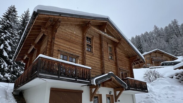 Un chalet en bois doté d’un toit à pente, de balcons en bois et surplombant un paysage enneigé.