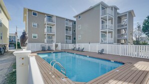 A swimming pool with a wooden deck, surrounded by a white fence, and adjacent to multi-story buildings with balconies. - Steps to Ocean: Water-View Carolina Beach Unit! (Carolina Beach)