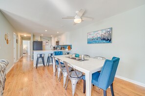 A modern kitchen with white cabinets, a central island, and blue bar stools. - Steps to Ocean: Water-View Carolina Beach Unit! (Carolina Beach)