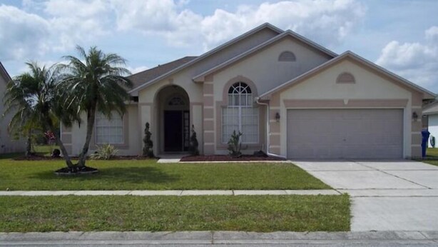 A two-story house with a garage, a front entrance with a door and a window, and a small lawn with a palm tree. - Cozy single-family home, close to theme parks, restaurants. Give Kids the World. (Kissimmee)