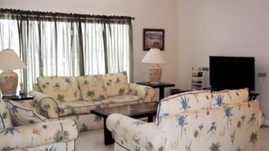 A living room with a sofa set, two lamps, a television, and a window with curtains. - Cozy single-family home, close to theme parks, restaurants. Give Kids the World. (Kissimmee)