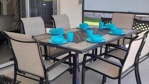 A dining area with a glass table and chairs, a projector screen, and a view of the outdoors. - Cozy single-family home, close to theme parks, restaurants. Give Kids the World. (Kissimmee)