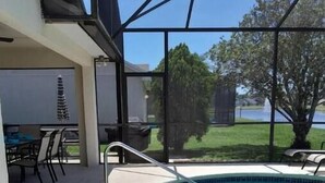 A swimming pool with a glass enclosure, a patio area with chairs, and a view of a lake and trees. - Cozy single-family home, close to theme parks, restaurants. Give Kids the World. (Kissimmee)