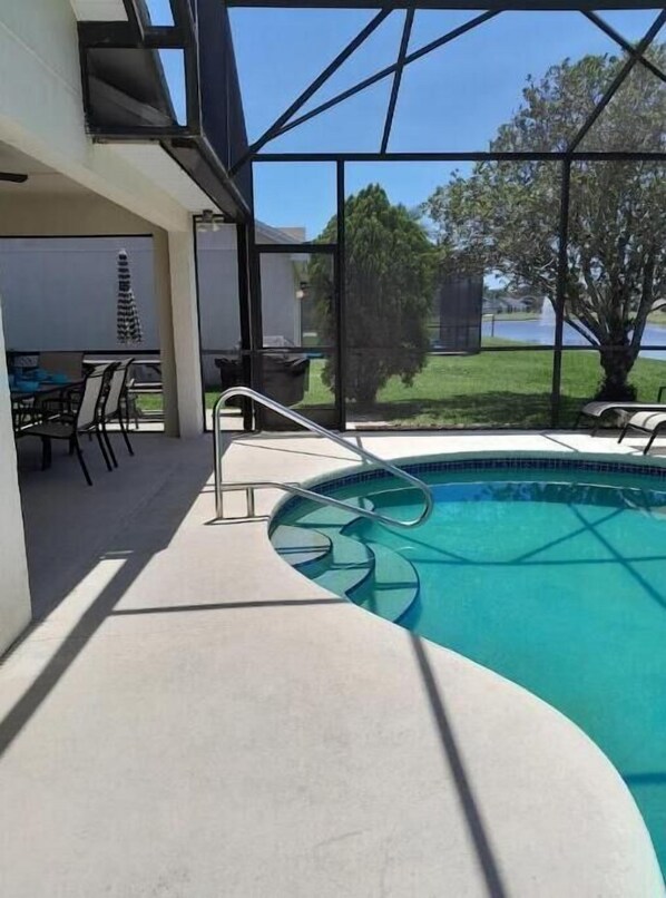 A swimming pool with a glass enclosure, a patio area with chairs, and a view of a lake and trees. - Cozy single-family home, close to theme parks, restaurants. Give Kids the World. (Kissimmee)