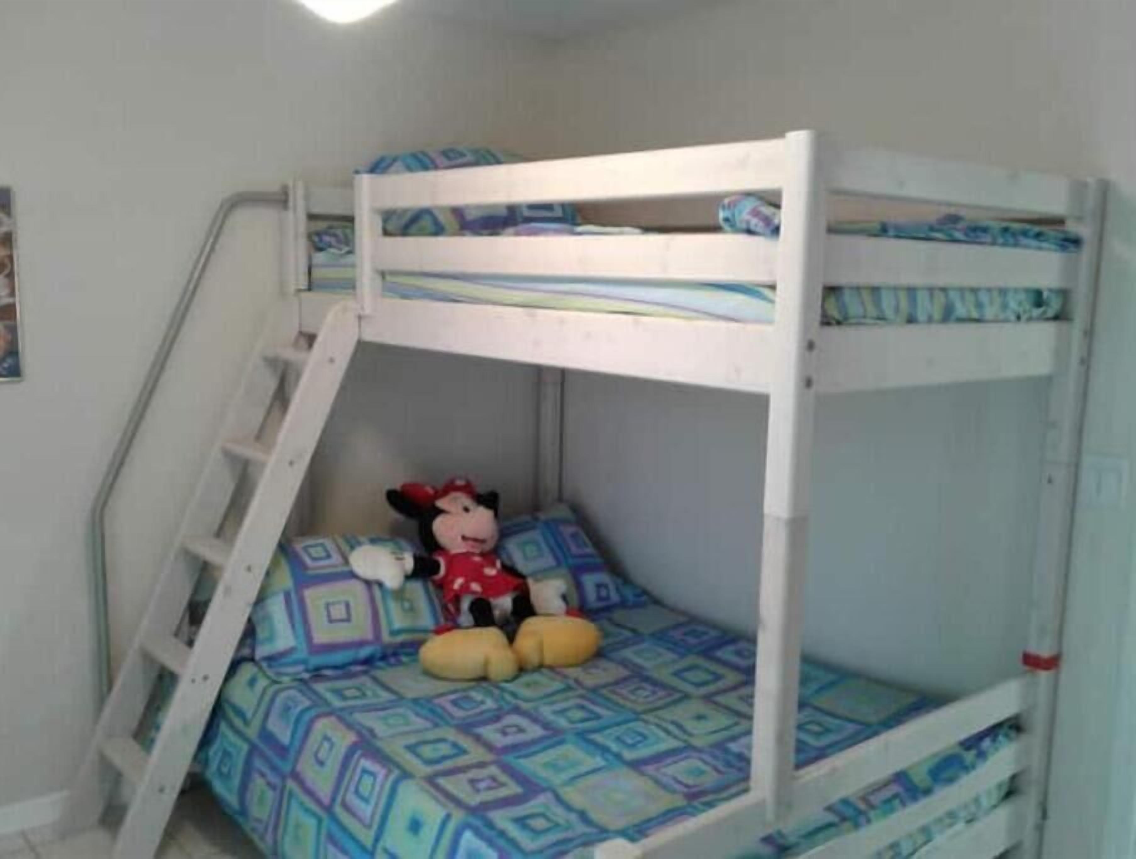 A bunk bed with a ladder, a Mickey Mouse plush toy, and patterned bedding.