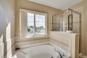 Une salle de bain dotée d’une grande baignoire, d’une douche à parois de verre et d’une fenêtre donnant sur l’extérieur.