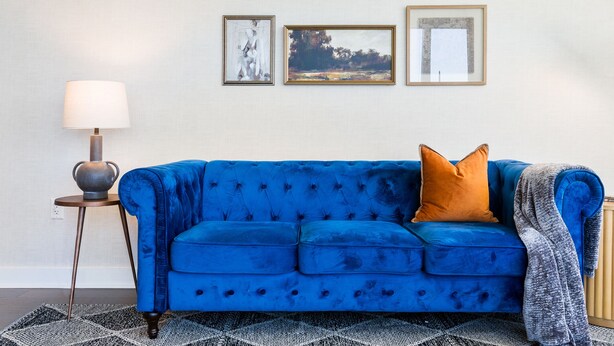 Un sofá azul con un cojín, una lámpara y tres cuadros en la pared.