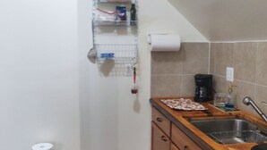 Una cocina con armarios de madera, un lavamanos, una cafetera y una estantería con varios objetos.