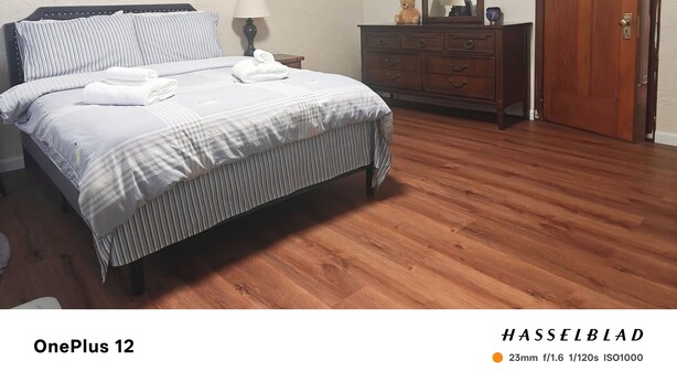 Una cama bien tendida con ropa de cama a rayas, un aparador de madera con espejo y una puerta de madera.