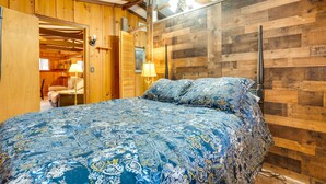 Una camera da letto con soffitto in legno, un letto con copripiumino decorato, un comodino con lampada e una parete in legno.