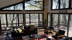 A spacious living room with large windows, a black leather sofa, a wooden coffee table, and a red patterned rug.