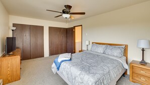 Un dormitorio con cama, armario de madera, ventilador de techo, mesita de noche y lámpara.