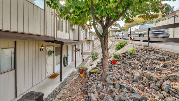 Una hilera de casas adosadas con un árbol en el patio delantero, un camino de entrada y un vehículo estacionado en la calle.