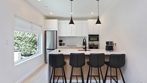 A modern kitchen with a central island, bar stools, stainless steel appliances, and pendant lighting. - Modern 2BR oceanfront apartment for sun, ski or mountain biking! (Courtenay)