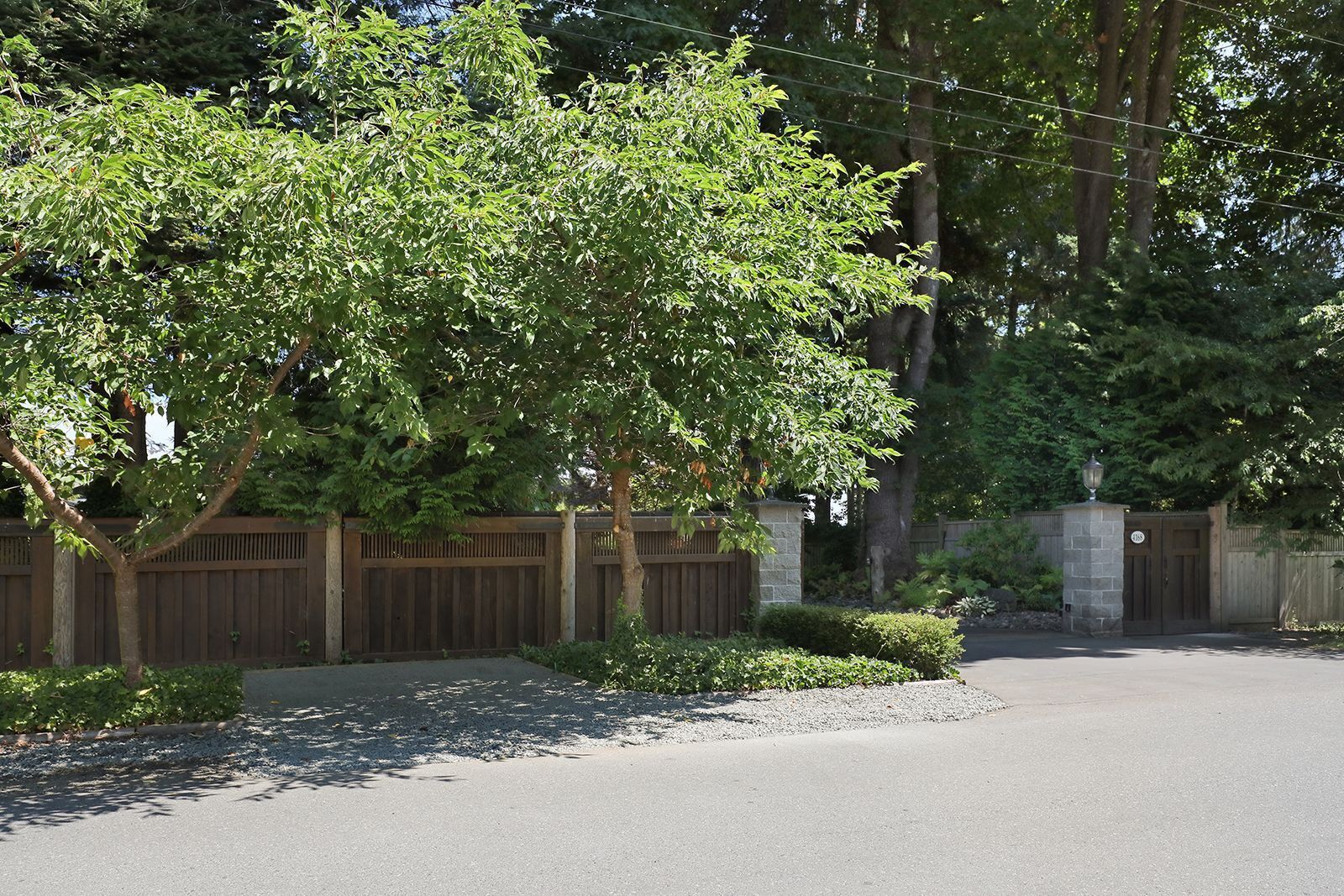 A residential driveway with a wooden fence, a gated entrance, and a well-maintained lawn.