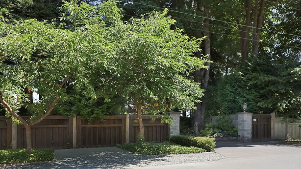 A residential driveway with a wooden fence, a gated entrance, and a well-maintained lawn.