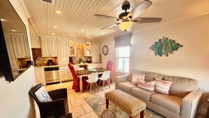 A modern kitchen with white cabinets, a dining area with a table and chairs, a sofa with cushions, and a ceiling fan. - Sunchase #303: Steps to Beach! Great View! (Gulf Shores)