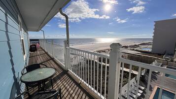 Uma varanda com vista para a praia e o oceano, uma piscina e móveis de exterior.