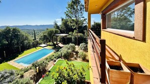 Una piscina con vistas a montañas, una terraza de madera y un edificio amarillo con una ventana.