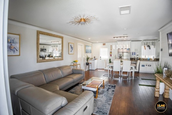 Living room,a cozy and stylish retreat with a plush neutral sofa, a patterned area rug, and a sleek coffee table. Soft wall colors and natural light create a warm ambiance,complemented by chandeliers. Personal touches include framed artwork, potted plants. It’s a perfect space for relaxation and entertaining.