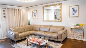 Un canapé d’angle en cuir beige, une table basse en verre, un grand miroir, des œuvres d’art encadrées et une petite table d’appoint agrémentée d’un objet décoratif.
