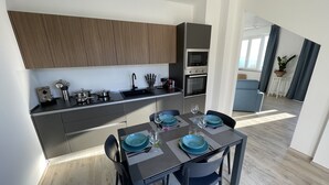 Una cuina moderna amb armaris foscos, una taula de dinar preparada amb plats blaus i vasos de vi, i vista a una zona de sala d'estar.