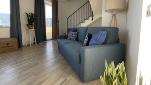 Un saló modern amb un sofà gris, una planta en test i una escala.