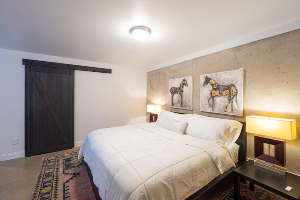 A bedroom with a bed, two wall-mounted lamps, a rug, and a door.