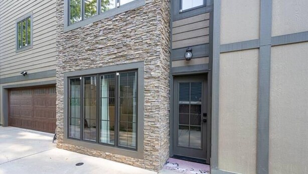 Une maison moderne à deux étages, dotée d’une façade en pierre, de grandes portes-fenêtres coulissantes et d’un garage.