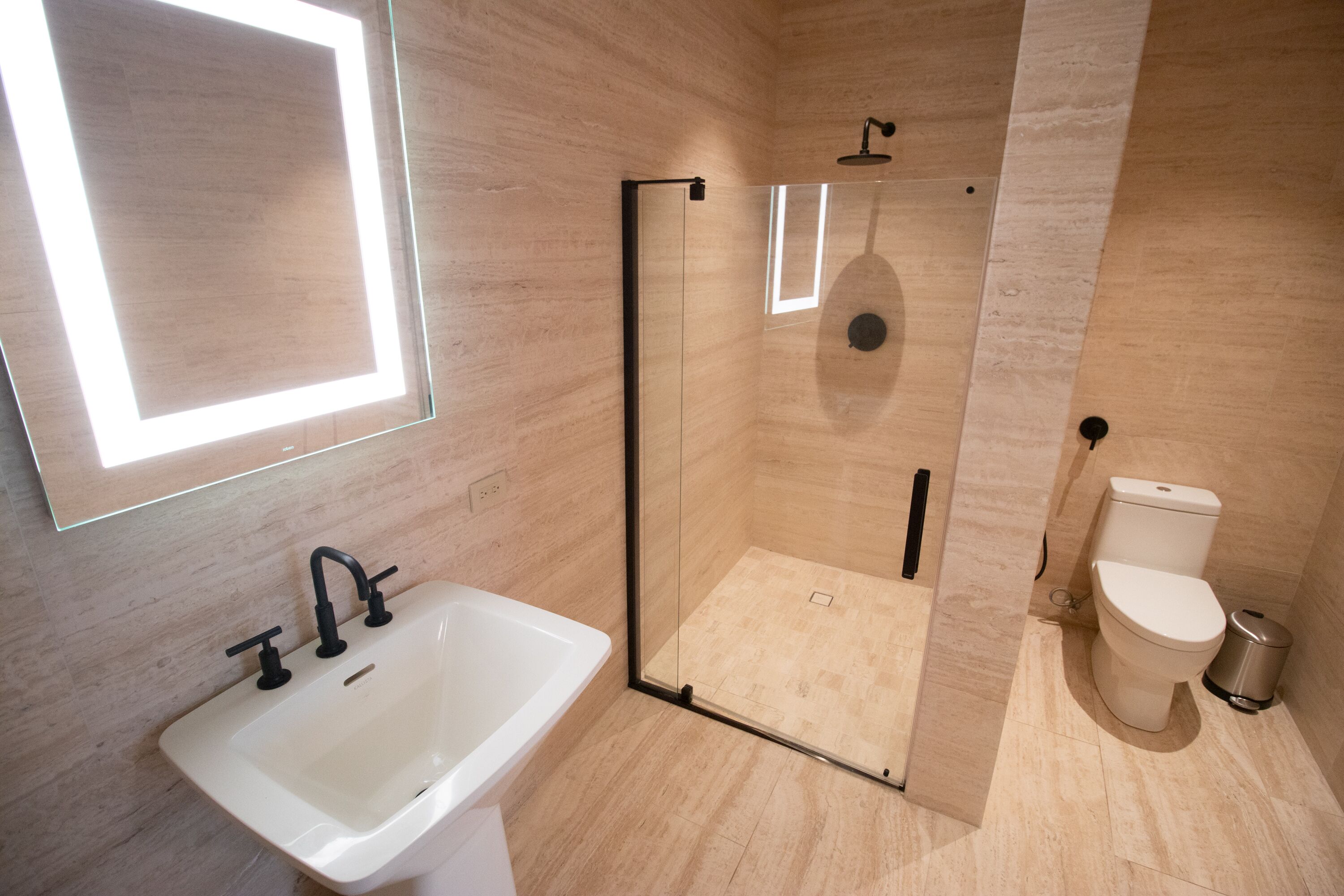 Un baño moderno con ducha de vidrio, lavamanos blanco y retrete.