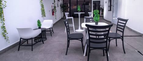 Un patio con una combinación de sillas y mesas blancas y negras, algunas con plantas en macetas.