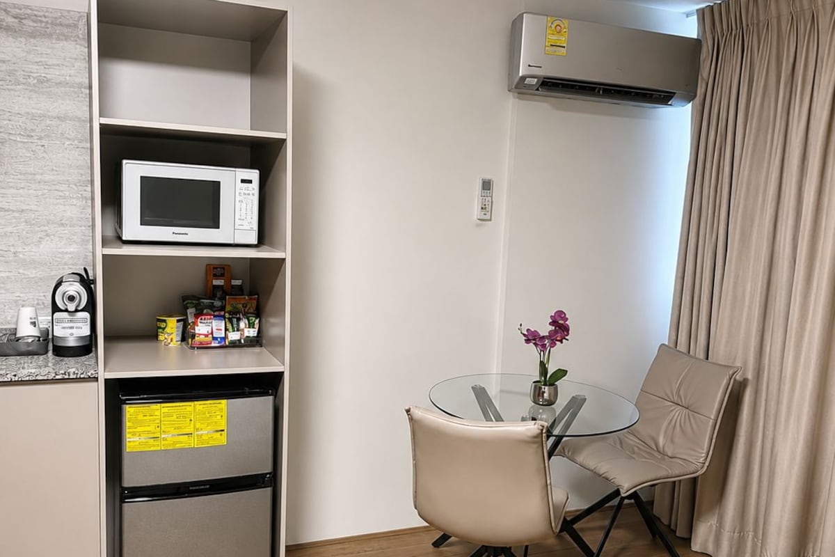 Een compacte hotelkamer met een kitchenette, een zithoek met een tafel en stoelen, een bed en een airconditioning.