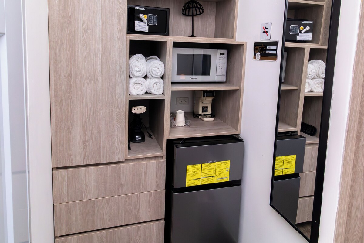 A compact hotel room with a built-in wardrobe, a minibar, a microwave, and a small refrigerator.