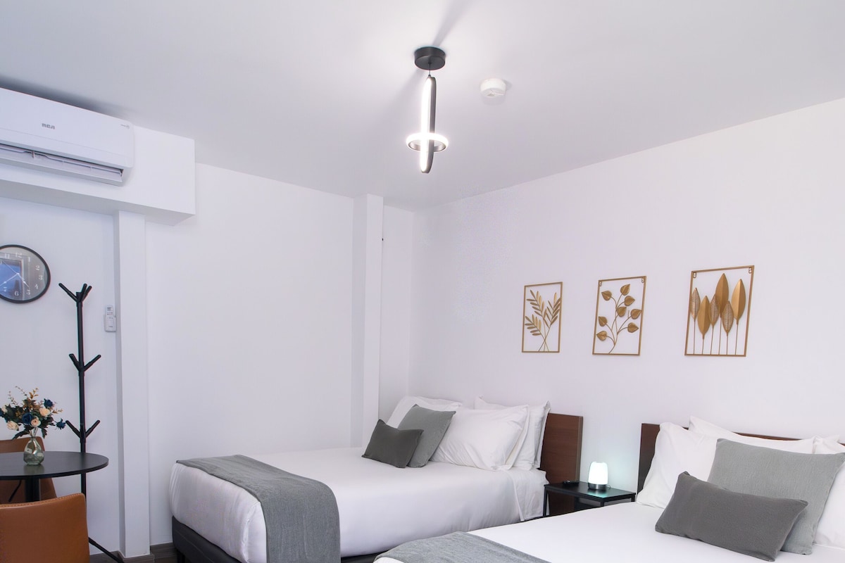 A hotel room with two beds, a desk, a chair, and a clock on the wall.