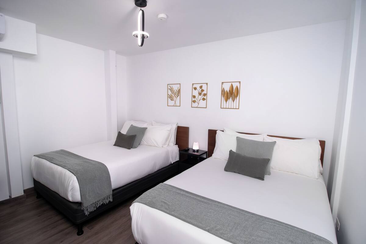 A hotel room with two beds, a bedside table with a lamp, and wall art.
