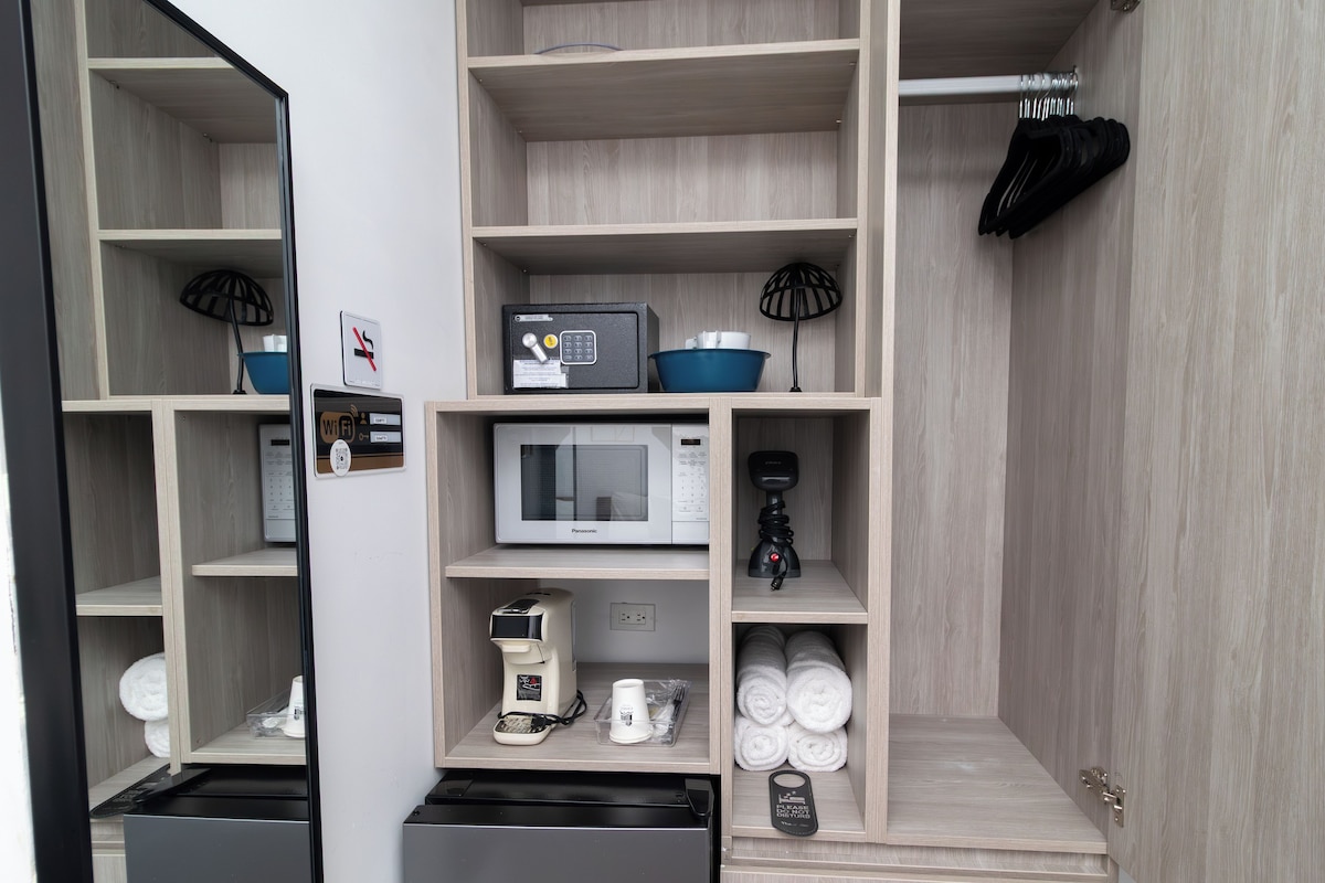 Een compacte hotelkamer met kitchenette, een magnetron, koffiezetapparaat en netjes opgevouwen handdoeken.