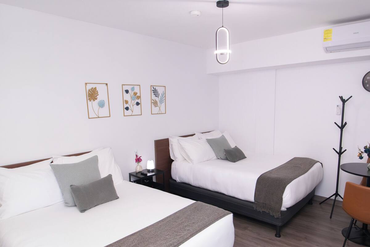 A hotel room with two beds, a desk, a chair, and a coat rack.