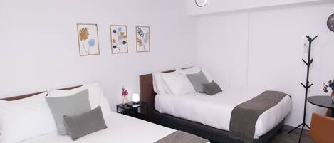 A hotel room with two beds, a desk, a chair, and a coat rack.