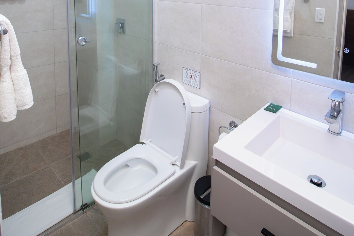 Een moderne badkamer met een douchecabine van glas, een wit toilet en een wastafel met een spiegel.