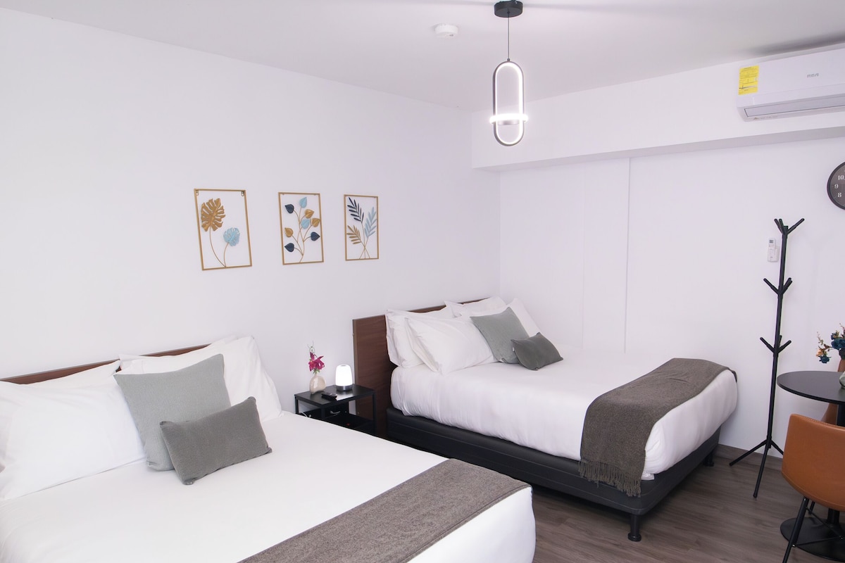 A hotel room with two beds, a desk, a chair, and a coat rack.