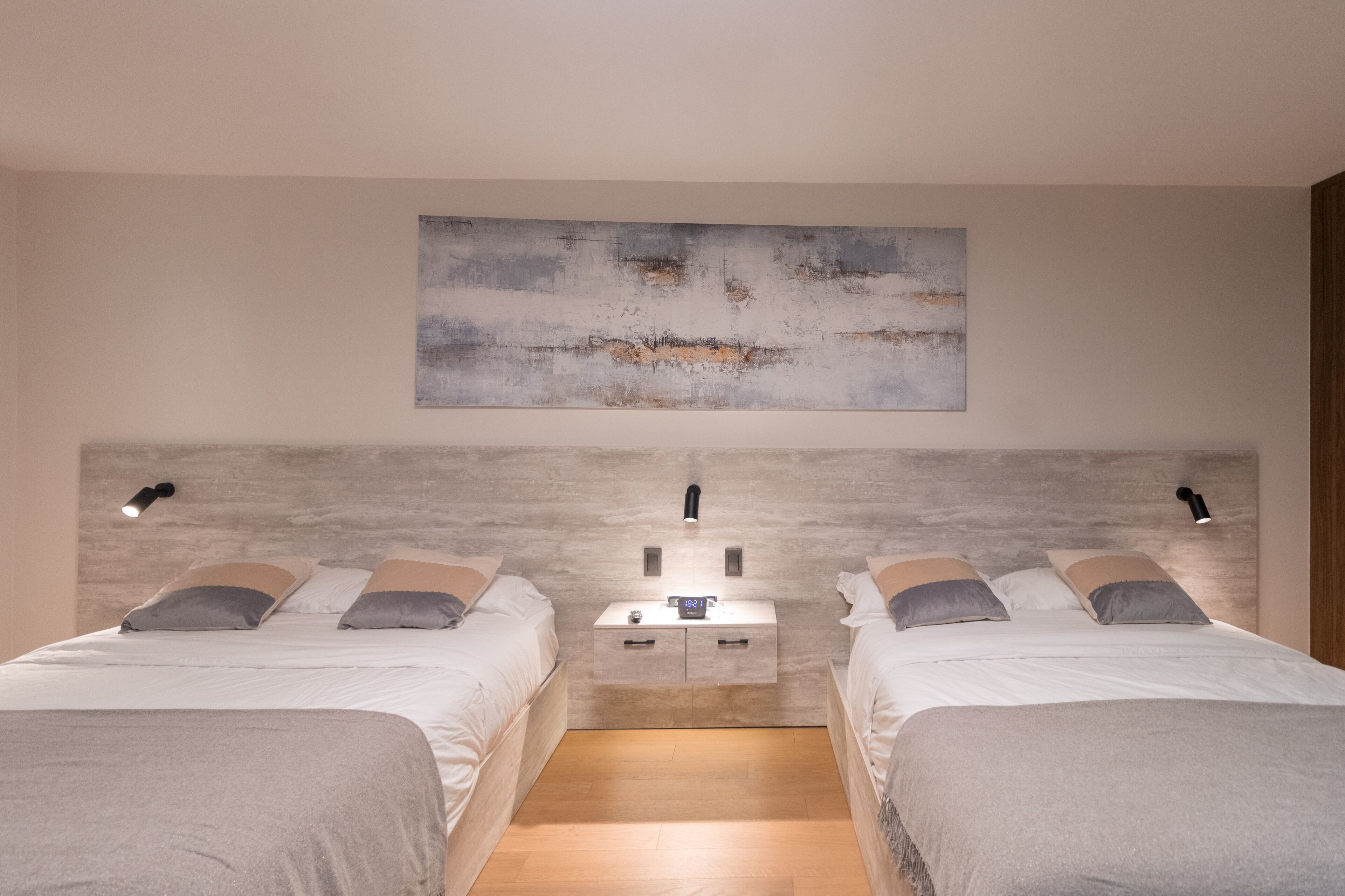 Une chambre moderne avec deux lits, une table de chevet et une œuvre d’art accrochée au mur.