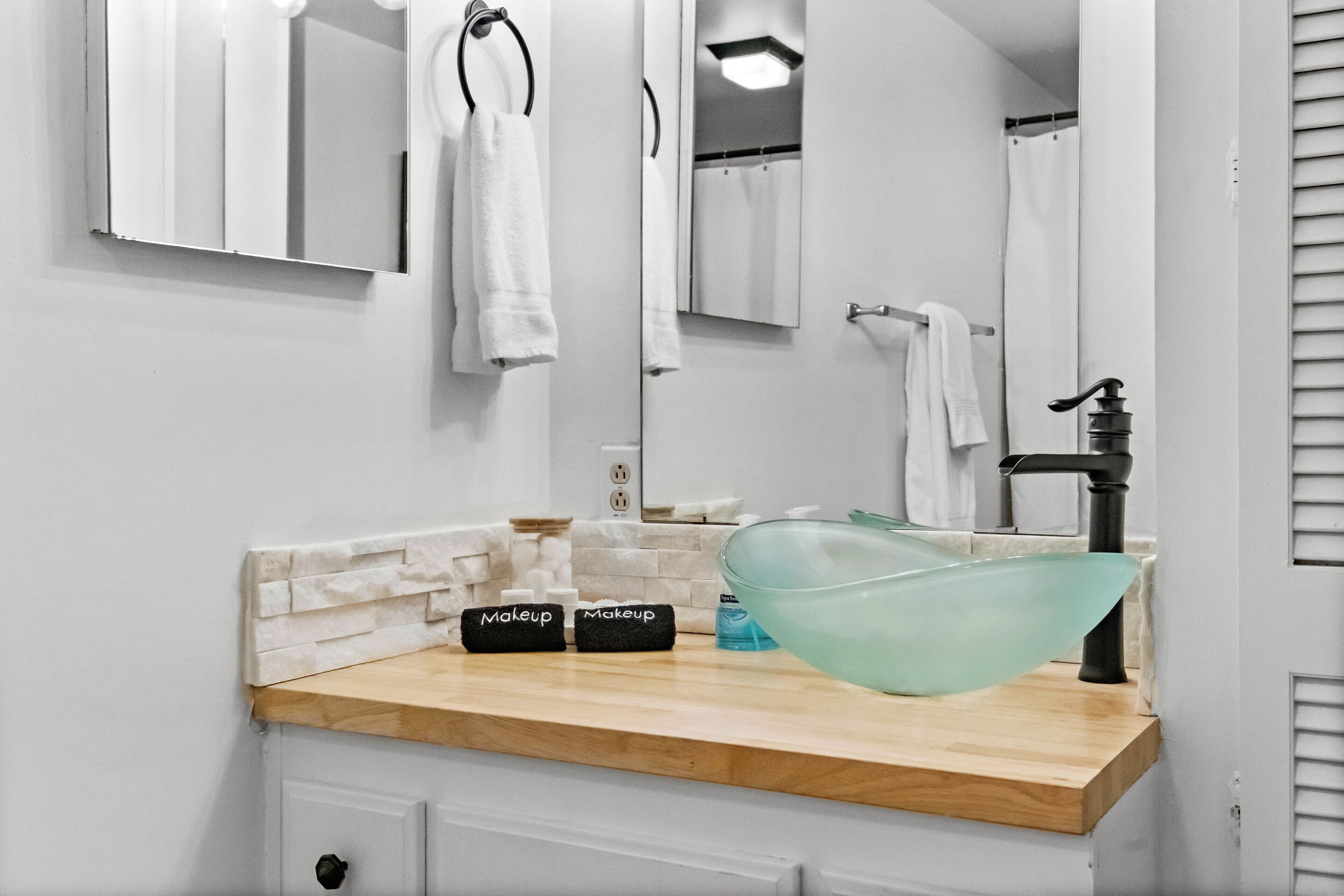 Un bagno con un lavandino bianco, un ampio specchio e una ciotola di vetro.