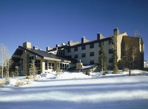 A multi-story building with large windows and a stone facade, surrounded by snow and trees.