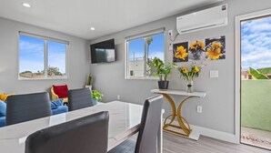 Un espace repas moderne avec une table blanche, des chaises noires et une petite console blanche agrémentée d’une plante.
